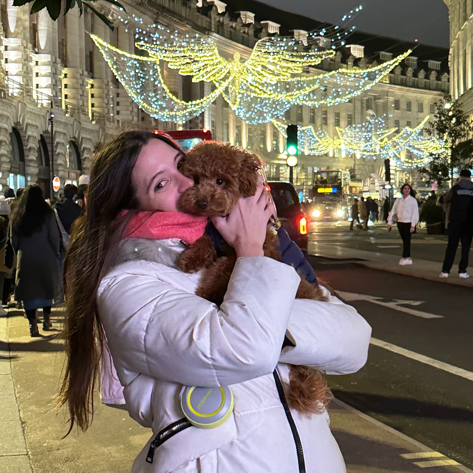 Woman holding a small brown dog in a city street with festive lights in the background